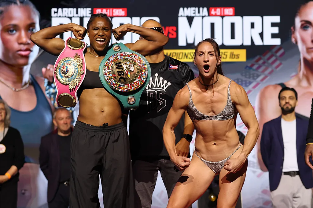 Caroline Dubois flexes with her WBC and WBO lightweight belts alongside Amelia Moore at the MVPW-06 weigh-in