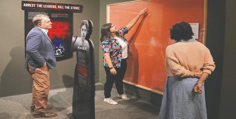 MDC’s Museum & Research Center Director Allyse Freeman (center) walks Andy Mink (left) and Smithsonian Institution’s Director of Regional Advancement & Outreach Jennifer M. Berges (right) through the permanent exhibit “Blue Collar Battleground: The Iron Range Labor Story.” This flag is a historical artifact from the 1916 labor march in Hibbing.