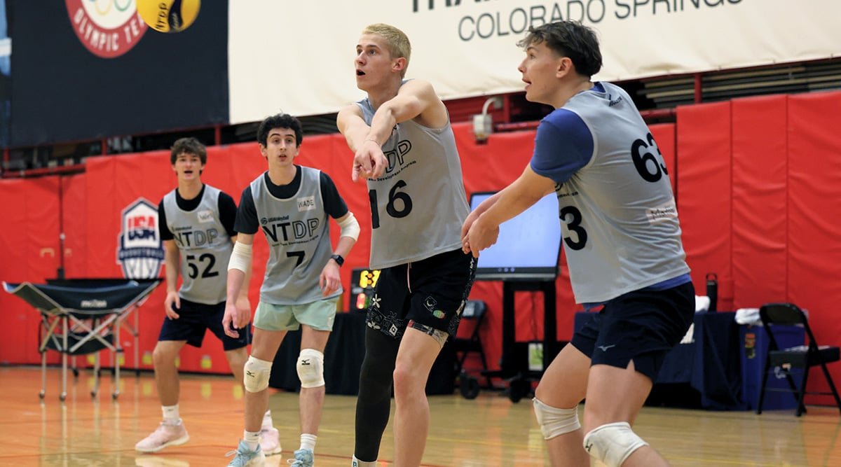 A boys volleyball player passes the ball while playing next to three others on the court