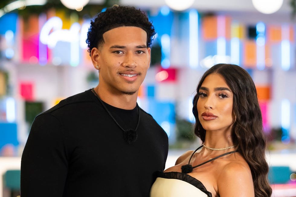 A couple posing together, smiling, in a colorful indoor setting with greenery and soft lighting.