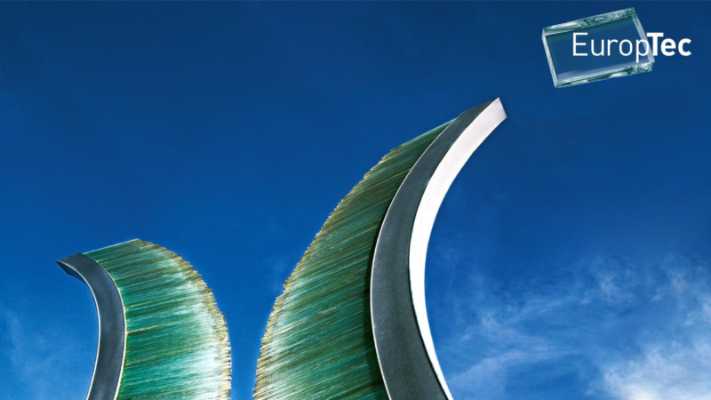 Two tall, curved sculptures made of stacked green-tinted glass panes edged in polished metal, rising like waves against a deep blue sky with light clouds. The EuropTec logo, set on a translucent glass block, appears in the top right corner