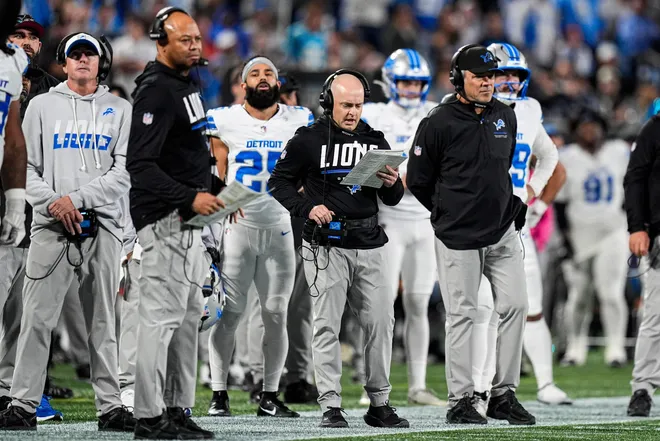 Detroit Lions offensive coordinator Drew Petzing, center, next to pass game specialist David Shaw, left, and quarterbacks coach Mark Brunel on the sideline before a play against the Carolina Panthers during the second half at Bank of America Stadium in Charlotte on Sunday, Oct. 4, 2026.